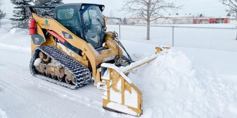 A grounds maintenance vehicle clearing snow on a road during winter.